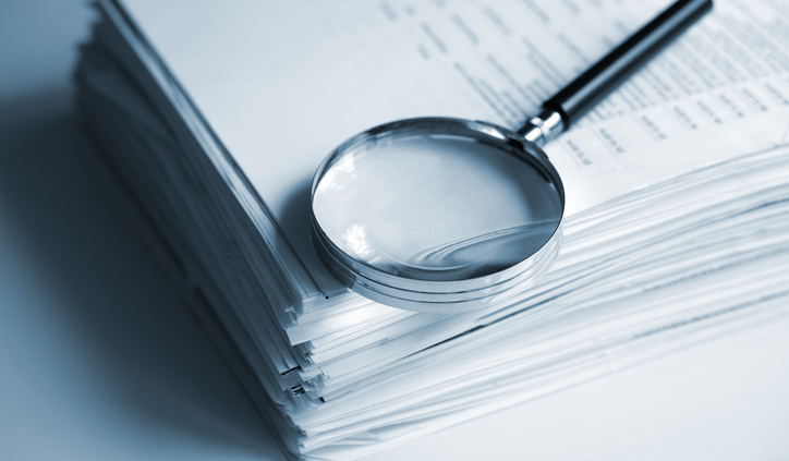 A magnifying glass rests on top of a stack of documents.