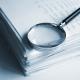 A magnifying glass rests on top of a stack of documents.
