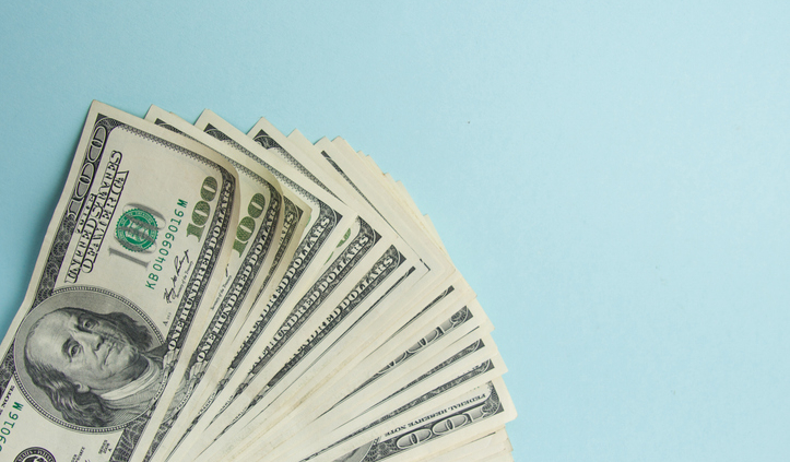 Stack of hundred dollar bills laid against a blue background, representing the income statement difference in owner's draw vs salary.