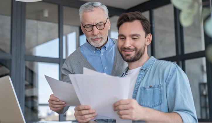 Father and son at a table, holding papers and examining them.