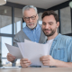 Father and son at a table, holding papers and examining them.